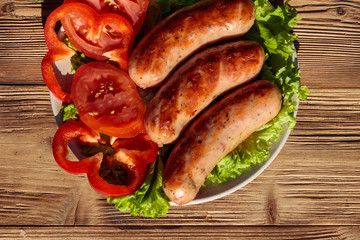 Grilled sausages with fresh vegetables on wooden table