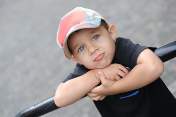 Portrait of a young boy with a cool face on the street. A boy stands on the stairs and leans on the railing