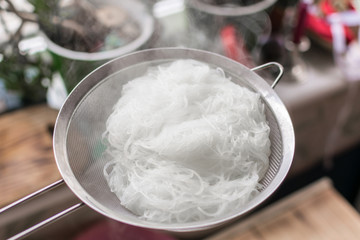 Boiled hot steaming rice noodles, spaghetti in a colander.