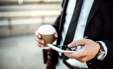 A close-up of a businessman with smartphone and coffee in the city, texting.