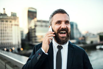 Laughing hipster businessman with smartphone in the city, making a phone call.