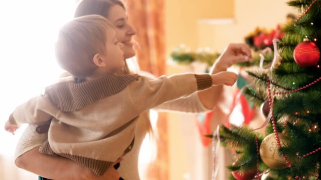 Happy young mother with her little boy decorating Christmas tree in living room