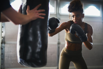 african woman boxing with punching bag in garage gym - Powered by Adobe