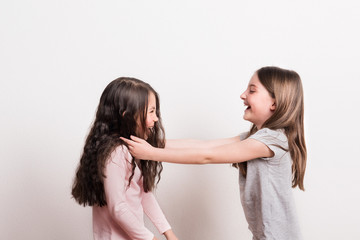 Two small girls standing opposite each other in a studio, laughing.