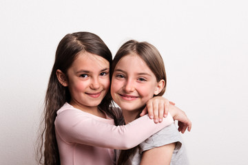 Two small girls standing in a studio., hugging.