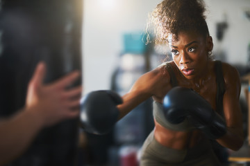 african american woman striking punching bag in home gym - Powered by Adobe