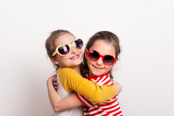 Small girls with sunglasses standing in a studio, hugging.