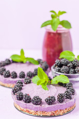 Raw blackberry dessert decorated with fresh ripe forest berries and green mint leaves and blended smoothie.