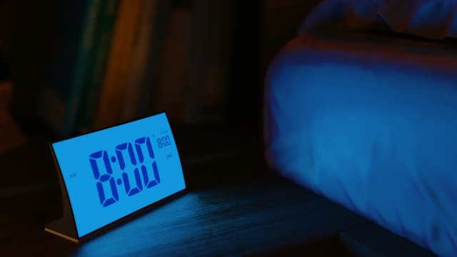 Digital alarm clock in a bedroom waking up at 8 AM. Close-up view. The clock screen is switching on for two seconds, then switching off for one second and go on