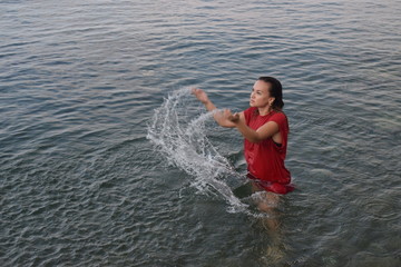 The girl in red bathes in the sea and splashes water.