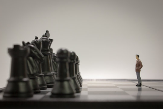 Closeup miniature businessman watching back chess side on chess board side view.	