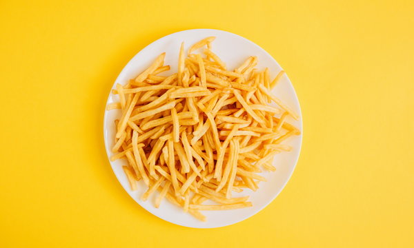 French fries on yellow background. Potatoes fries in the on white plate. Flat lay, top view, copy space 