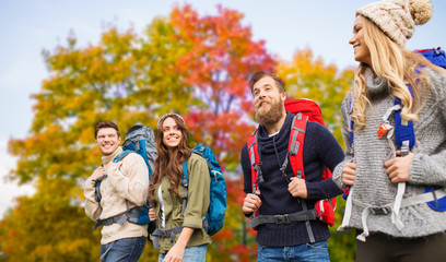 Fototapeta premium travel, tourism, hike and people concept - group of smiling friends with backpacks hiking over autumn trees background
