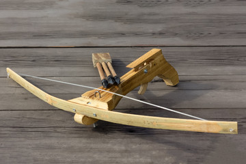 A wooden toy crossbow with a set of bolts lies on a dark wooden background