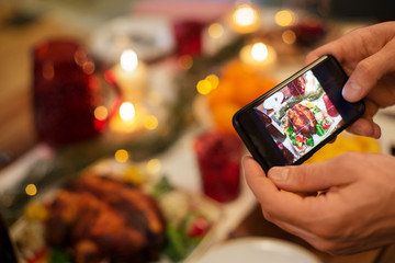 food, technology and holidays concept - close up of male hands photographing roast turkey by smartphone at christmas dinner