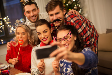 holidays and celebration concept - happy friends with party props taking selfie by smartphone at...