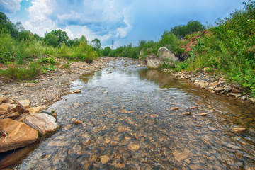 Mountain river stream of water in the rocks with majestic blue sky.