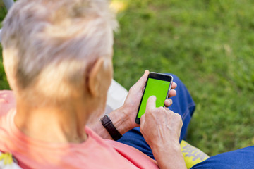 back view of senior old man hands scrolling on the phone with chroma green screen on summer day