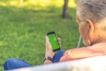 back view of senior retired man browsing the internet with phone with a green screen