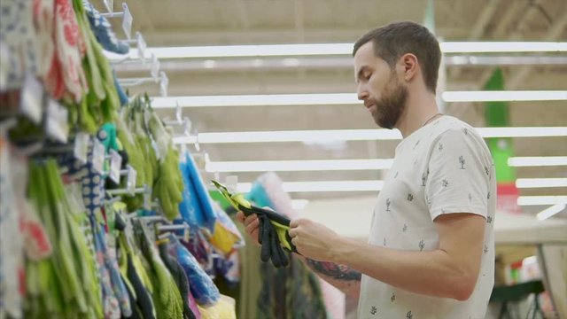Man is groping rubber gloves for gardening works in a shop. He is touching and checking materials of goods
