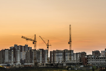 Fototapeta premium building site with three tower cranes against the background of multi-storey houses and a orange sky, night scene