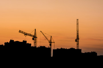 the silhouettes of three tower cranes and houses during sunset, sunset with an orange sky in the city
