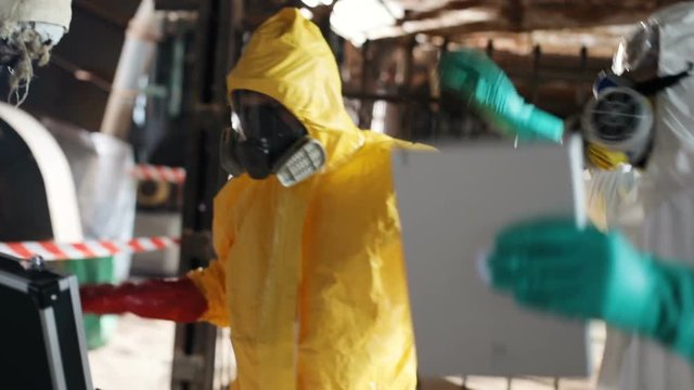 Two scientists in colored hazmat outfits dancing weirdly. Guy in white protective suit holding digital tablet in hand. Indoors. Danger.
