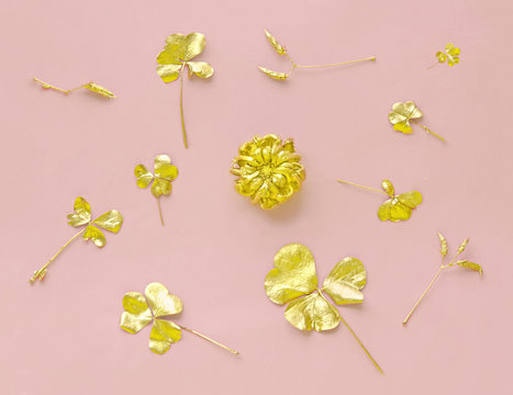 Golden flower and clover leaves on pastel pink paper background. Autumn creative concept. Top view.