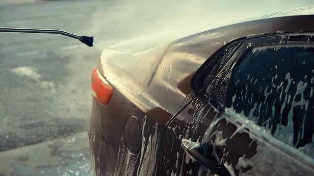 Car getting washed outside using water jet, high pressure, shiny car. Clean car, foam on car body.