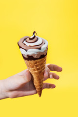 chocolate cream ice cream in waffle cone on yellow background.