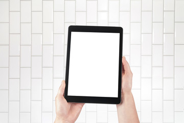 Hands holding tablet and brick tiles stacked in the background. Internal room such as a hospital, spa, bathroom, butcher's shop or toilet. Isolated screen with copy space.