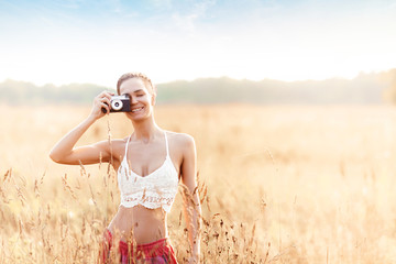 Young attractive girl with camera in field at sunset