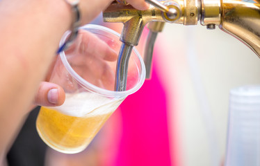A bartender serving beer at a dispenser in plastic glasses