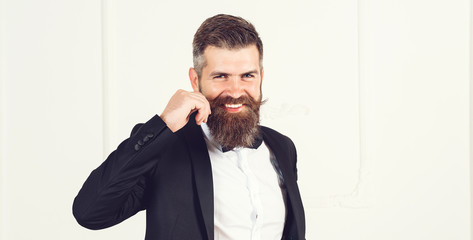 arrogant smiling businessman with beard one hand twists his mustache stands near white wall