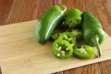 a group of jalapeño peppers one sliced on a natural cutting board with writing space