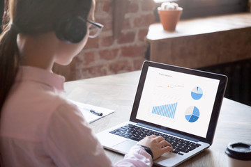 Businesswoman with headphones working, analyzing financial graphs on laptop in office. Woman...