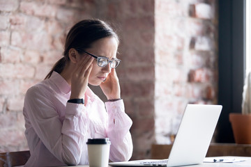 Young tired woman in eyeglasses working at office. Eyes fatigue, migraine and headaches at work...