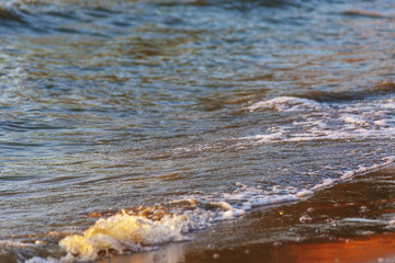 Waves on the sandy shore of a large river. The rays of light are reflected in the waves.
