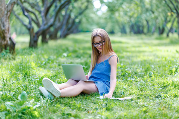 Young woman with notebook in park looking at laptop