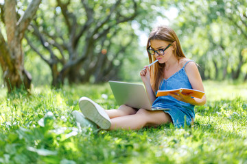 Young woman with notebook in park looking at laptop