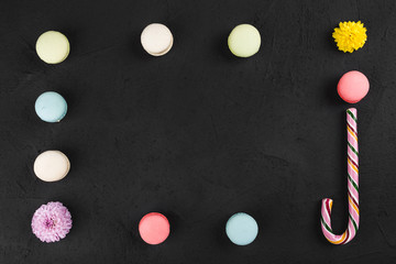 Colorful macaroons, lollipop and flowers on black stone table. Sweet macarons. Top view with copy space