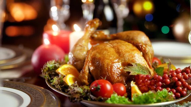 Closeup 4k footage of baked chicken with vegetables on Christmas dinner. Burning fireplace and glowing Christmas lights on backgorund