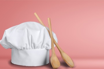 White cooks cap and wooden spoons on wooden table