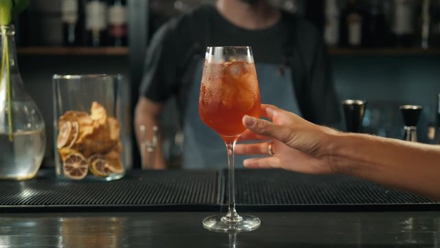 Woman hands toasting with aperol spritz cocktails, woman in bar take alcohol from bartender