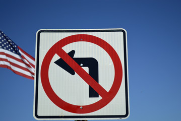 A no left turn sign with an american flag in the blue sky background