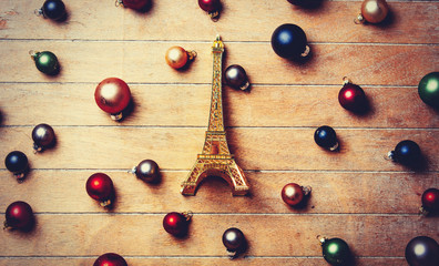 Eiffel tower souvenir with Christmas baubles around on wooden table. Above view in old color style
