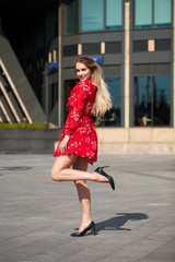 Sexy blonde model posing on th street in red summer dress