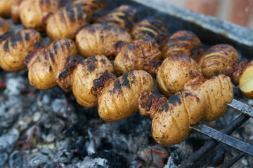 Baked potato with lamb fat on skewer over coals