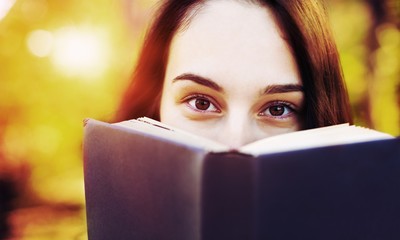 Young woman reading book in city park at summer day