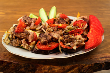 Meat dish with baked eggplant, tomato, zucchini and onion, wooden background.